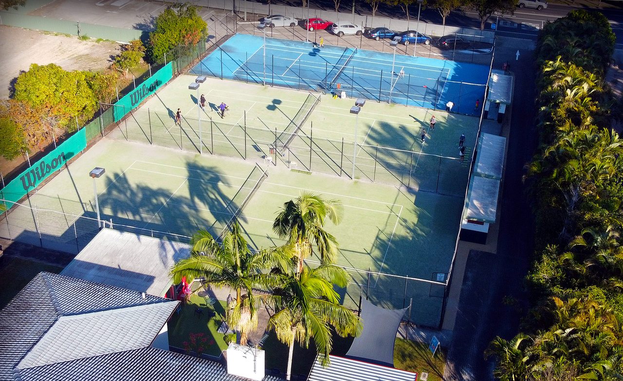 Aerial view of the three floodlit courts and clubhouse at Logan Tennis Club