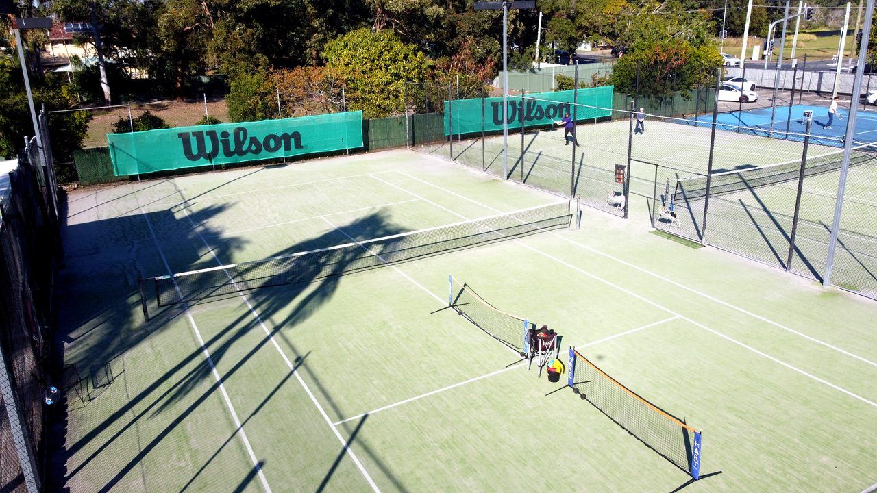 Elevated view of portable mini nets and ball baskets on a grass court, with neighbouring courts beyond the fence