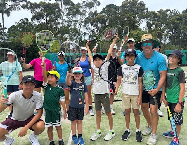 Children and teens holding racquets at a club clinic, with Paul Hanley in a straw hat on the right