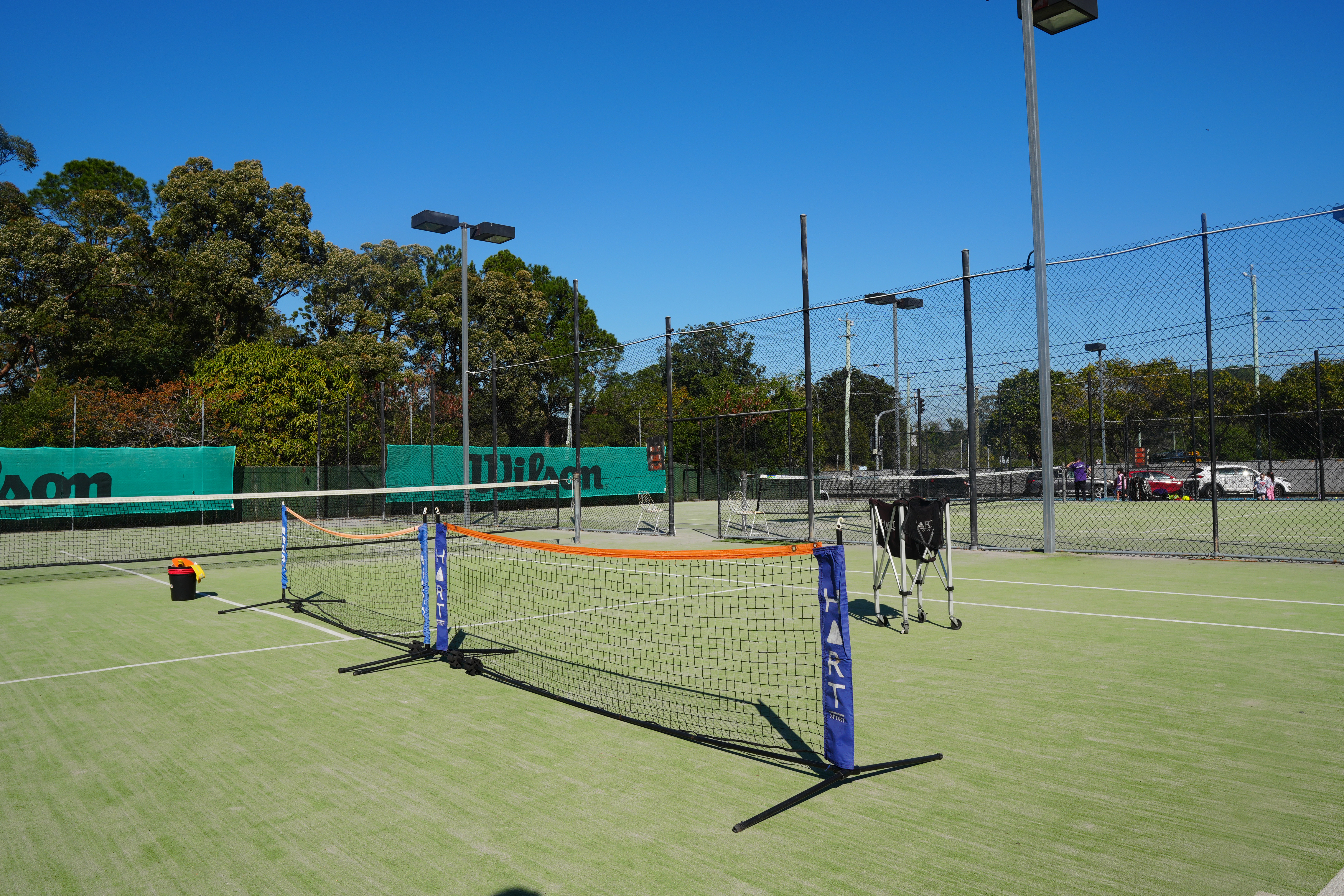 Two portable orange-topped mini nets and ball baskets set up on the synthetic grass court